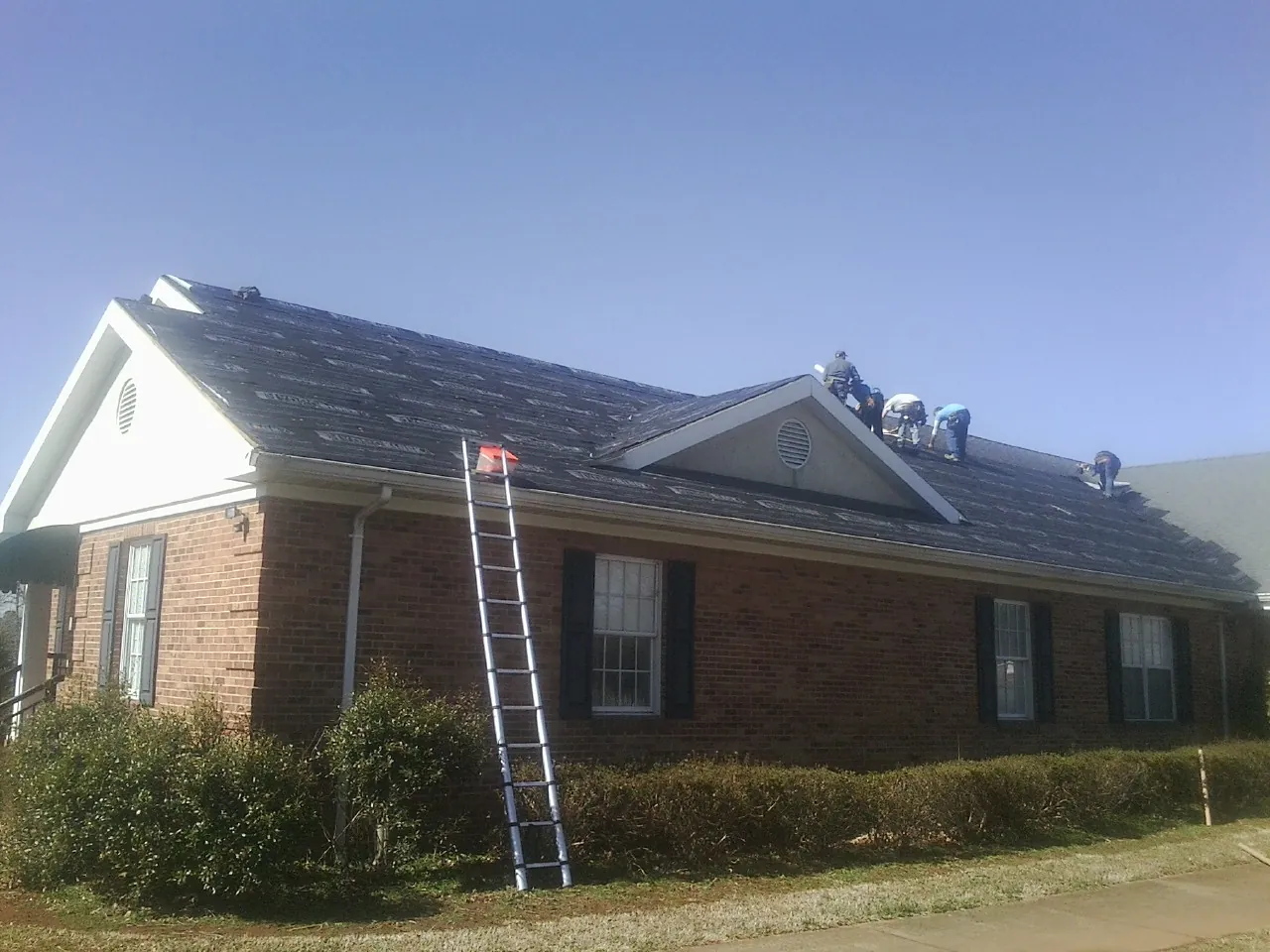 Crew tearing shingles off a brick ranch roof with a ladder set — Metal Roof Repair work by our crew in Beavercreek