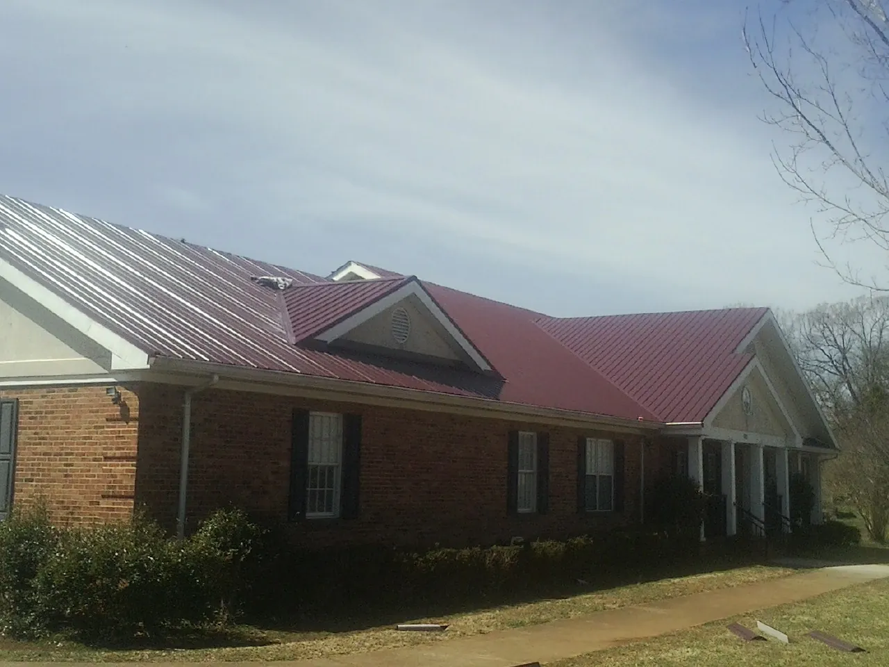 Red metal roof with gabled entries on a long brick building, from a Hail Damage Roof Repair job in Beavercreek