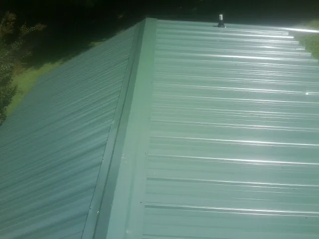 New green metal panels meeting at the ridge of a roof — Flat Roof Repair work by our crew in Beavercreek