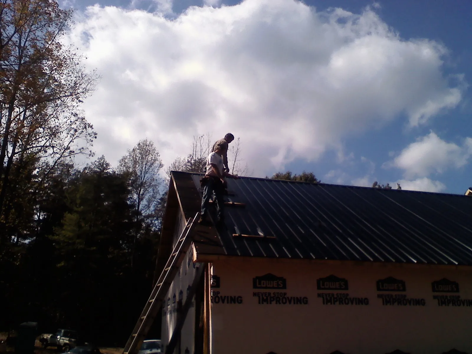 Roofer fastening dark metal panels high against a cloudy sky, from a Roof Inspection job in Beavercreek