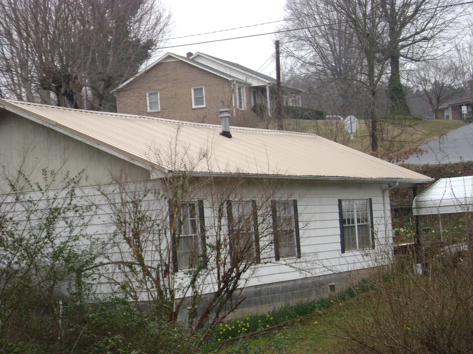 Tan metal roof on a white sided house set into a hillside — Commercial Roofing by Roofing Brothers in Beavercreek